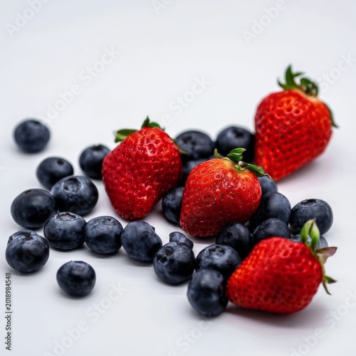 Fresh Strawberries and Blueberries Scattered on a White Surface for a Healthy...