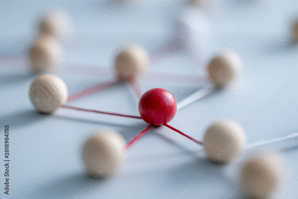 Obraz premium A red wooden sphere as a central hub in a network of connections. Concept of leadership, teamwork, and standing out from the crowd