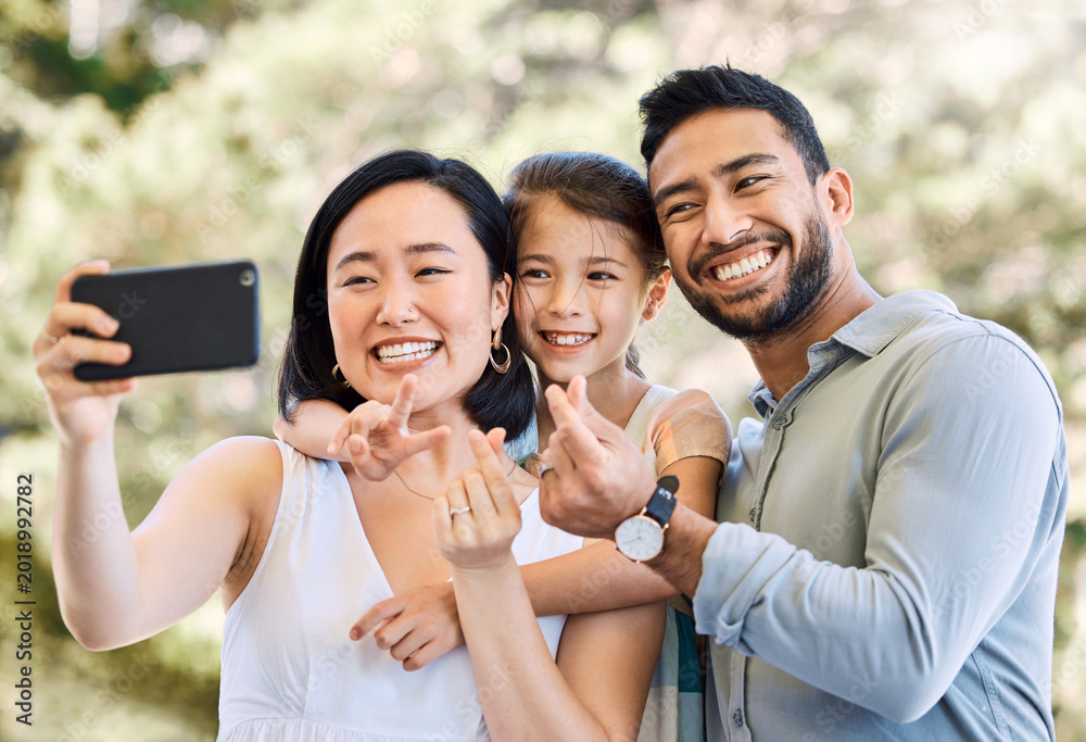 Fototapeta premium Parents, child and outdoor with peace sign for selfie, travel memory and bonding on summer holiday. Asian family, excited and photography in park for vacation blog, love and heart emoji with daughter