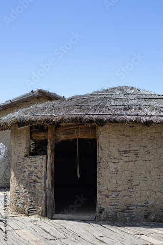 hut with a thatched roof in a reconstruction village, capturing ancient architectural history under a clear blue sky on a wooden pier.