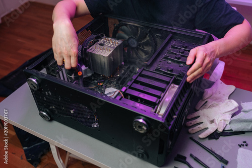 Person hands removing components from an open desktop computer case on desk, performing maintenance and upgrades with tools while inspecting internal hardware and wiring.