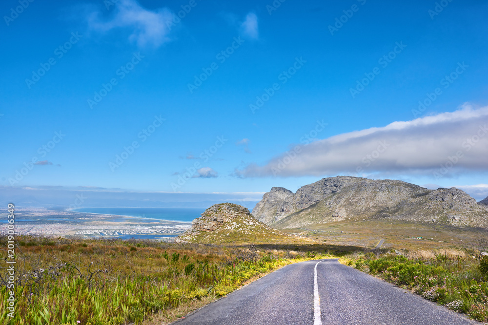 Obraz premium Travel, blue sky and road on mountain to ocean, tourist destination and journey outdoor. Landscape, background and street with scenic route, highway and space for vacation, trip and holiday to coast