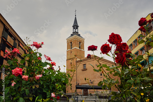 Fotografi Bell tower of San Salvador Church in Leganes, Madrid, with red roses in the foreground