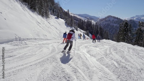 Descending winter mountain with colorful skiers. Mountain skiers carving turns under clear blue sky during winter. Group of skiers in vibrant jackets navigating groomed snowy piste on mountain resort