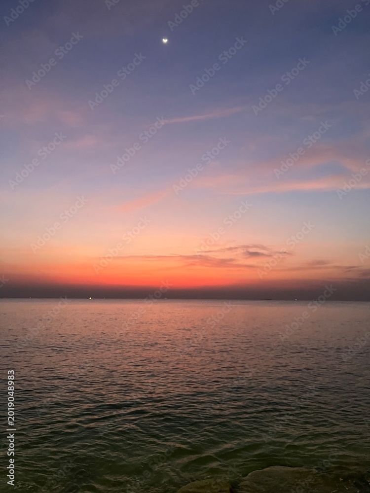 Obraz premium Colorful Sunset Seascape with Moon Over Calm Ocean Horizon