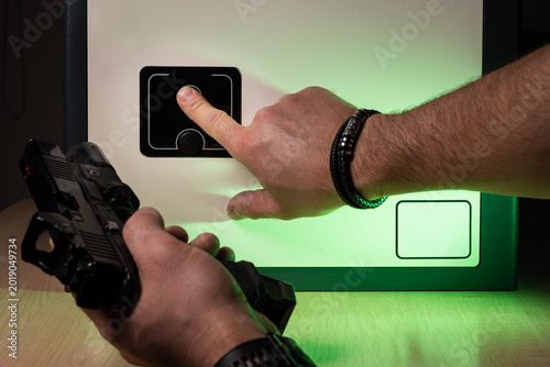 Man using biometric fingerprint scanner to open a modern home safe for secure handgun storage.