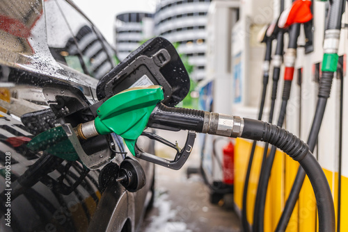 Canvastavla Refueling black car at gas station with green fuel nozzle on rainy day in German