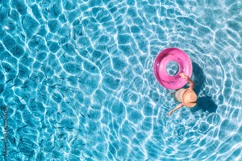 Schilderij op canvas Aerial drone view of a young woman in hat swimming with pink swim ring in blue sea with school of fish