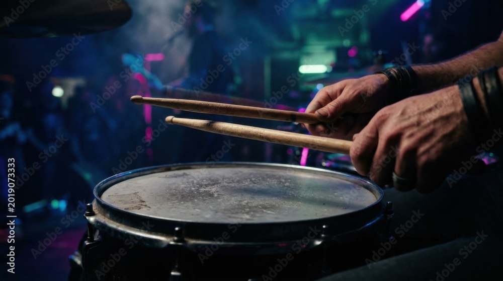 Obraz premium Focused image of hands gripping drumsticks over an aged snare with dust particles visible set against a dark smoky backdrop illuminated by cinematic neon lighting at a dynamic