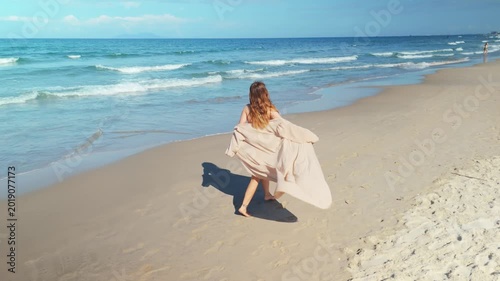 Woman running freely along the sandy beach shoreline with waves breaking, enjoying summer vacation and a leisurely escape by the ocean, captured with an aerial perspective