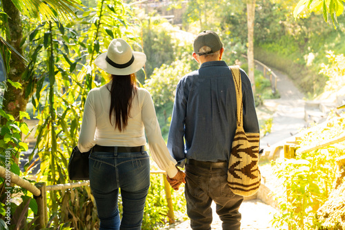 A  happy senior couple enjoys walking together through a beautiful eje cafetero park as colorful fall leaves and tall trees surround the happy couple and their children in nature