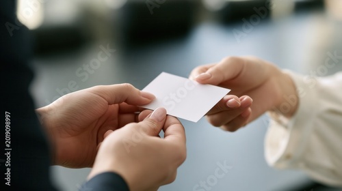 Close up of hands exchanging a blank white business card in a professional setting.
