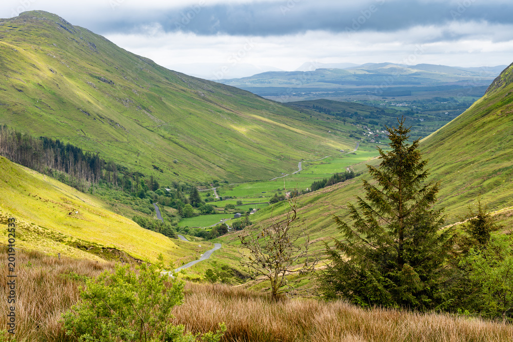 Obraz premium Glengesh Pass winding through a green mountain valley in County Donegal, Ireland. A scenic road landscape of the Wild Atlantic Way and remote Irish highlands.