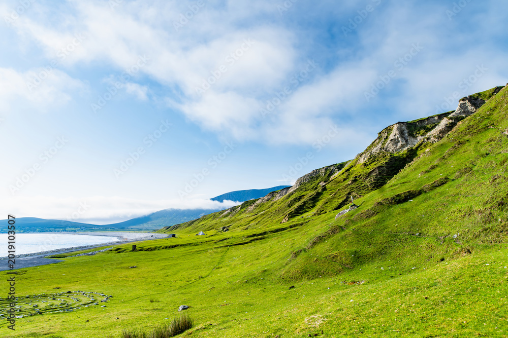 Fototapeta premium Southern Keel Beach on Achill Island, County Mayo, Ireland, with green coastal slopes above the shore. This image shows the quieter grassy edge of the beach.