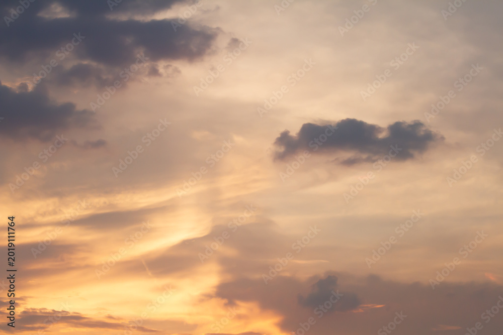 Obraz premium Gentle pastel clouds stretch across a glowing sunset sky with warm light and subtle atmospheric textures, creating a serene natural background at twilight.