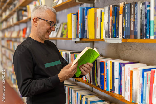 Foto Mature man reading book discovering knowledge in library