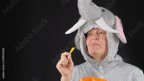 Middle-aged woman in an elephant costume eating potato chips. In a good mood. Enjoying. On a black background.