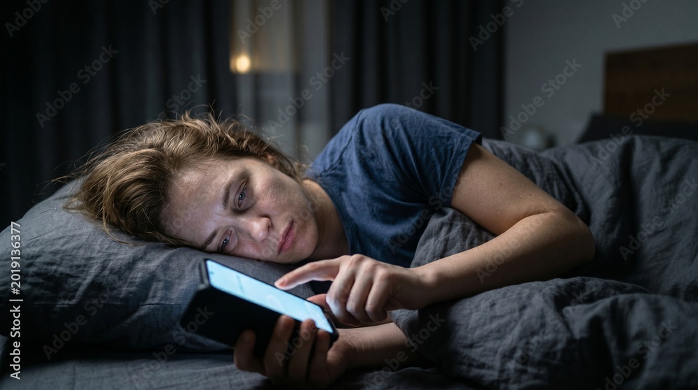 Obraz premium Tired woman lying in bed using smartphone at night for social media