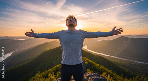 Happy man standing with open arms on mountain top at beautiful sunrise perfect for freedom and active travel goals