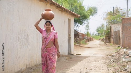 Indian woman walking on dirt road carrying pot on her head  
