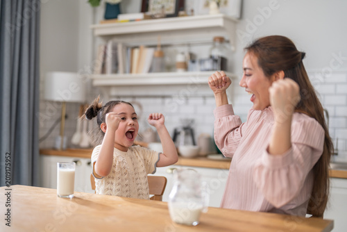 Asian happy mother and little daughter showing strong arms after drinking milk at breakfast, Smiling family enjoying healthy nutrition, protein and calcium for child development and growth concept