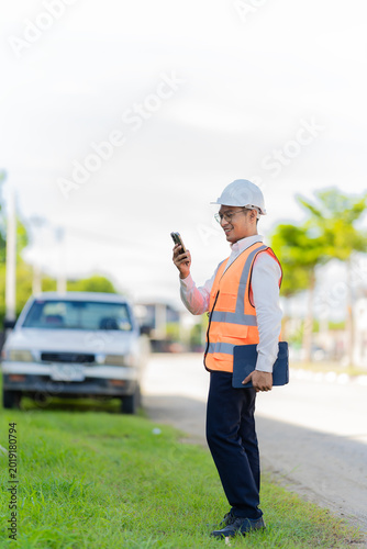 A male civil engineer or construction supervisor, wearing a yellow safety helmet and reflective vest, is on a construction site, representing a real estate development concept for a housing constructi