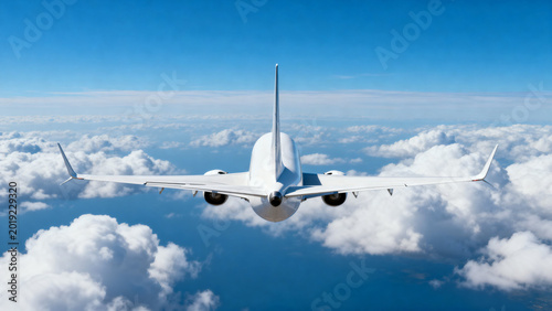 Rear back view of a modern white airplane Boeing 737 passenger jet flying away into the distant horizon surrounded by soft white clouds and clear blue sky air travel and aviation industry
