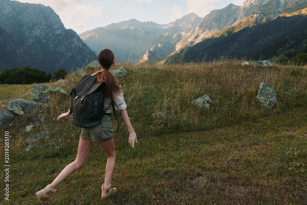Fototapeta premium A woman hiking with a backpack across a mountain meadow, exploring rugged landscape under clear skies. A lifestyle moment of outdoor adventure and nature connection.