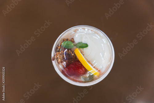 Top Down View of Healthy Yogurt Parfait with Fresh Strawberry, Lemon Slice, Granola, and Mint Garnish in a Clear Plastic Cup