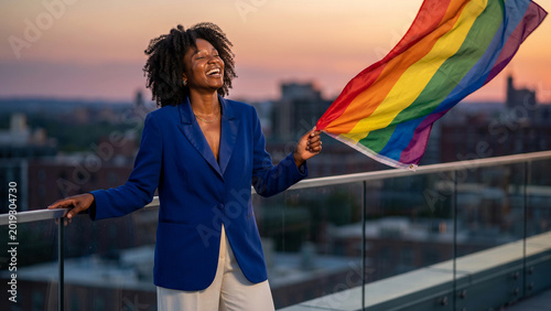 Joyful Black Woman Celebrating Pride with Rainbow Flag on City Rooftop at Sunset