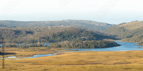 Tasmanian wilderness landscape with lake, golden grasslands and forested hills