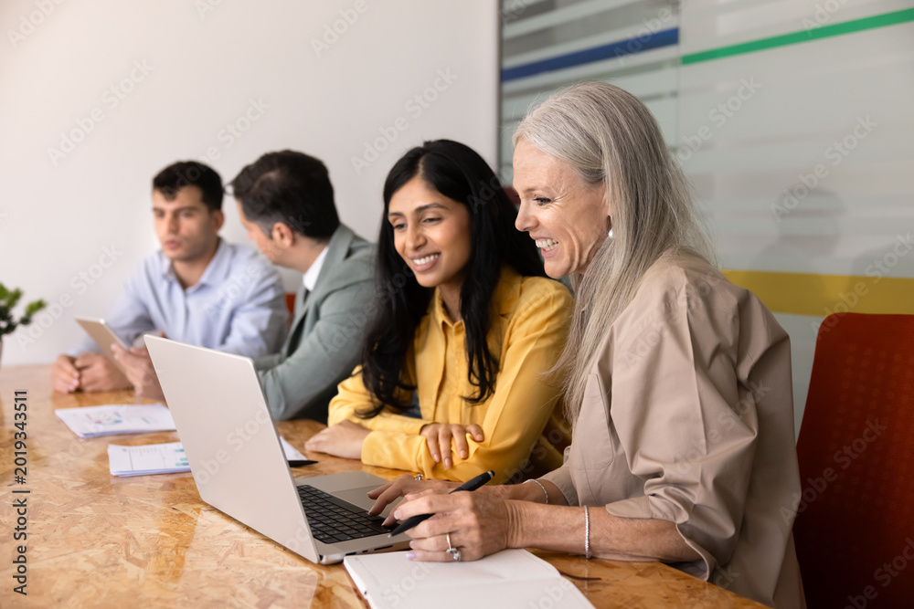 Fototapeta premium Multiethnic female colleagues working on laptop, discussing project details, reviewing data, planning strategy, team preparing business presentation, sharing ideas, collaborating in corporate office