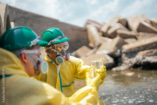 Water quality inspectors wearing protective equipment examine wastewater samples in industrial environment. Pollution testing and environmental monitoring help identify contamination risks.