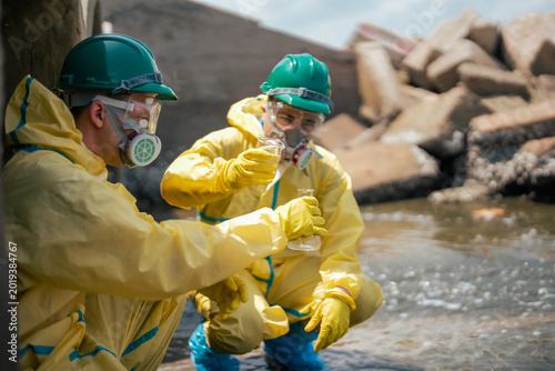 Scientists wearing full protective conduct wastewater testing and environmental analysis at an industrial drainage site, examining contaminated water samples for public health and ecosystem safety.