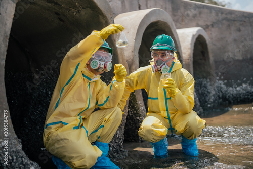 Billede på lærred Field researchers wearing safety gear gather polluted water samples from industrial drainage systems to evaluate contamination risks, and long-term environmental protection strategies