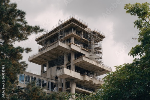 Unfinished concrete building with scaffolding and trees