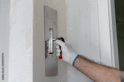 Photography Technician smoothing finishing coat on wall using a stainless steel trowel during renovation work