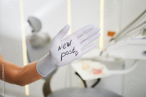 Dentist hand in glove shows New post text in dental office. Creative healthcare concept for clinic social media, online promotion, patient communication