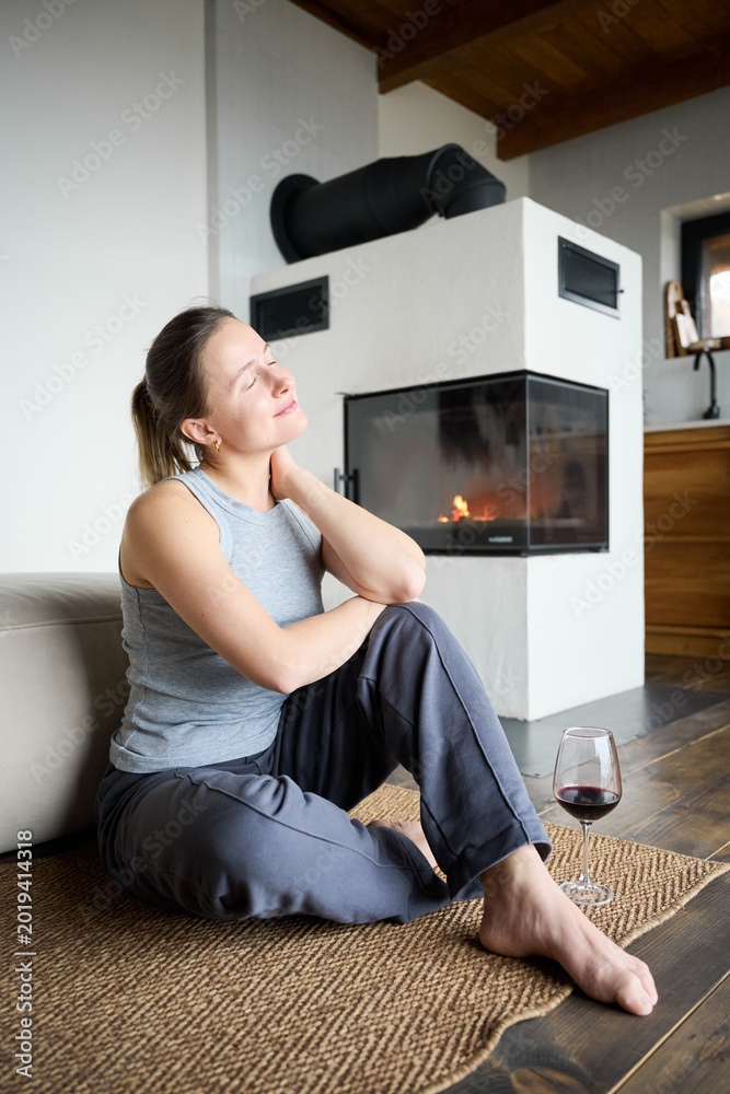 Fototapeta premium Woman unwinding near fireplace with wine in hand, sitting on floor and enjoying peaceful, warm and inviting interior setting