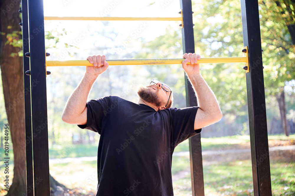 Obraz premium Man performs pull up on horizontal bar at outdoor gym in park. Active fitness scene for strength training, calisthenics, healthy lifestyle, sports motivation, or workout promotion