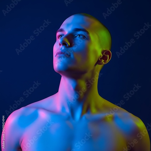 Young man with close-cropped hair gazes upward under contrasting colored illumination against a dark background