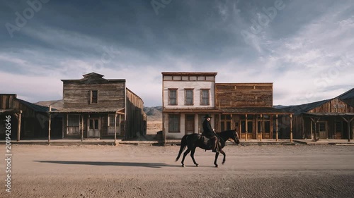 Lone rider on horseback traverses a dusty old western town street