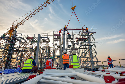 Construction workers assembling steel framework on building site at dusk