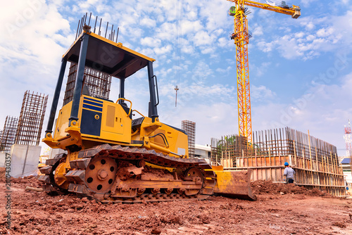 Yellow bulldozer operating at construction site with crane and fencing