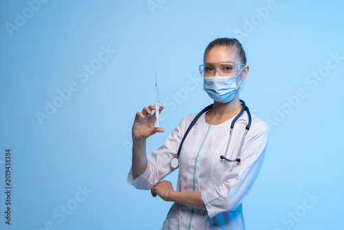 Female medical professional in white coat and mask preparing vaccine syringe for immunization against COVID-19, studio shot