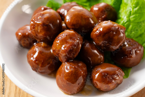 Meatballs with glossy brown sauce and green lettuce in a white bowl on wooden table background