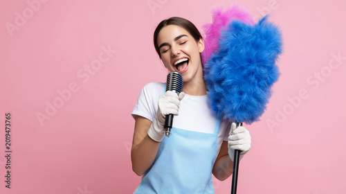 Young woman singing into a vintage microphone holding a colorful feather duster, enjoying cleaning and housework