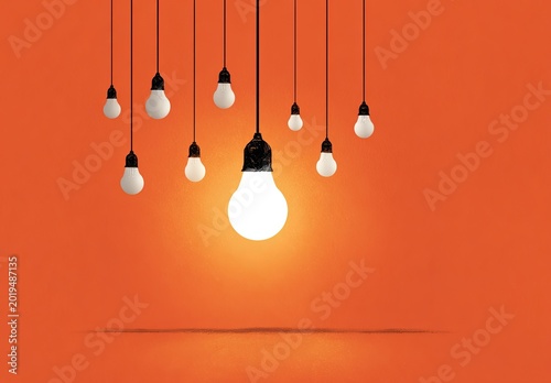 Bright lightbulb shines prominently among others against an orange background
