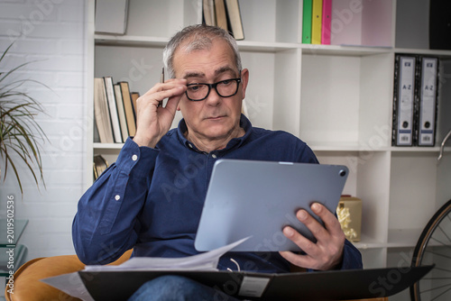 An elderly man using glasses struggles to read the news on a digital tablet