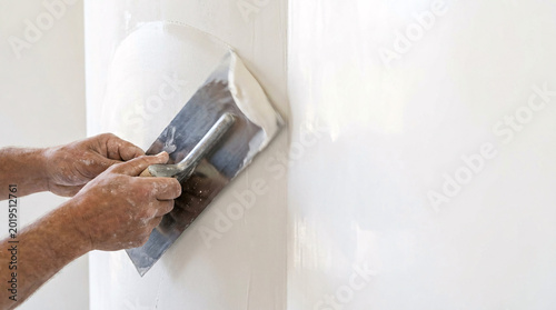 A person applying putty to a wall surface using a putty knife indoors.